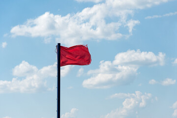 Against the background of a blue cloudy sky, a red shabby torn old flag develops, a clear sunny day - a danger signal, a warning