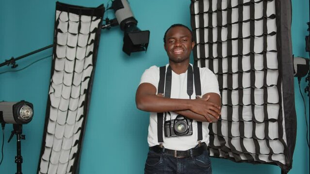 African american man having backstage photography equipment, using spotlight, flashlight, dslr camera lens and tripod. Photographer posing with creative tools in studio behind the scenes.
