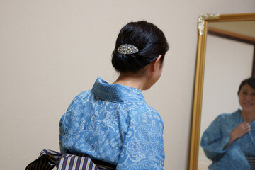 鏡の前で浴衣(絹紅梅)の着付けをする中年女性の後ろ姿