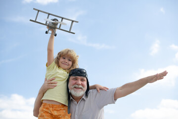 Grandfather and son having fun with plane outdoor on sky background with copy space. Child dreams of flying, happy childhood with granddad. Golden age.