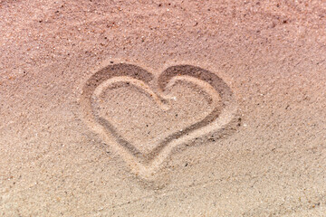 Evening pink light, drawn symbol of heart, love on light yellow sand, beach