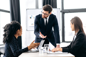 Fototapeta premium Elegant Caucasian intelligent male boss, holding group brainstorm with female colleagues, discussing ideas for a new business project, analyzes report and profit, explain info