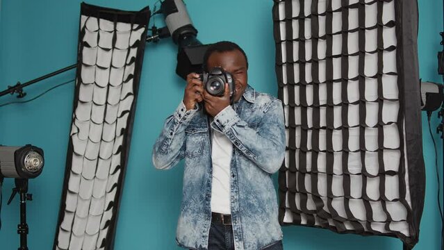 Male photographer using dslr camera and lens to take pictures in studio backstage, capturing photos with professional equipment. Using focused view to photograph images over background.