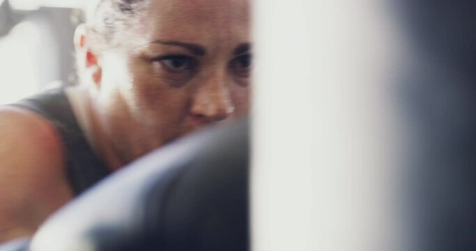 Active and real woman hitting a punching bag in real life at the gym to lose weight. Sweaty, candid and serious athletic female or normal person doing a boxing exercise to improve cardio and fitness