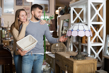 Loving couple looking for stylish table lamp in shop of secondhand furniture