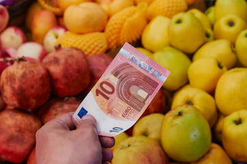 Buying fruits in the supermarket. the buyer gives money for the purchase. 10 euro banknote in hand. Apples, pomegranates, peaches and nectarines in the blur in the background