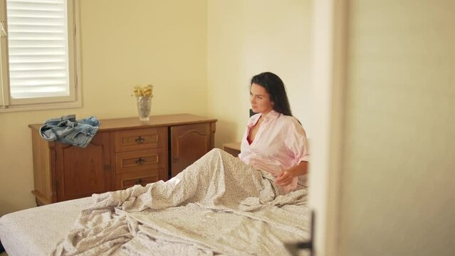 The girl wakes up in bed in the morning and stretches. A beautiful romantic woman in a shirt gets up from the bed in the apartment. High quality 4k footage