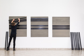 Woman artist assembling modern art installation on the art gallery wall