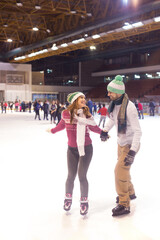 Young couple ice skating in the public ice skating rink in winter
