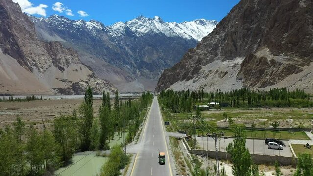 Cinematic drone shot of Passu Cones in Hunza Pakistan, Tuk Tuk driving on Karakoram Highway with Tupopdan Peak in the background