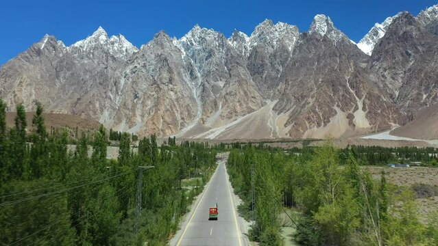 Cinematic drone shot of Passu Cones in Hunza Pakistan, moving towards the Tupopdan Peak tracking a Tuk Tuk driving on Karakoram Highway, aerial shot