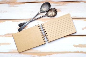 Blank recipe book and vintage spoon, top view. blank notepad for recipe on white board table. Place...