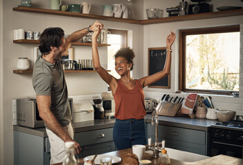 Happy interracial couple dancing, having fun and bonding together in the kitchen at home. Carefree,...