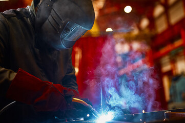Laborer in protective mask welds manually metal frame