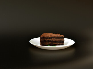 A plate with a piece of chocolate cake decorated with mint leaves on a black background.