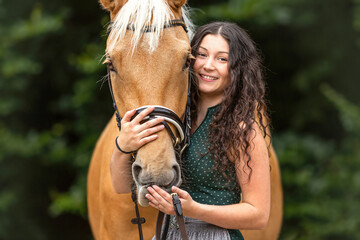 Portrait of a female equestrian nearby her horse. A young woman cuddles with her palomino kinsky warmblood horse - obrazy, fototapety, plakaty