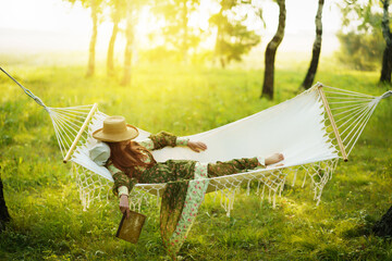 Woman with hat resting in comfortable hammock at green garden.