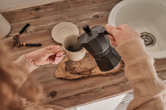 From Above Of Crop Anonymous Female In Warm Sweater Pouring Hot Coffee From Geyser Coffeemaker Into Cup In Kitchen