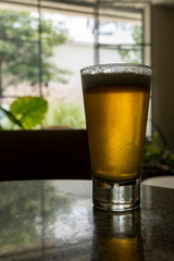 glass of beer on a terrazzo table, two yellow chairs in the background, retro table, window with natural light