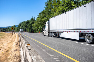 Convoy of different big rigs semi trucks with semi trailers running long haul freights on the wide interstate highway road