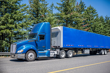 Day cab blue big rig semi truck with roof spoiler transporting cargo in blue dry van semi trailer...