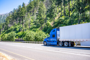 Long haul blue big rig semi truck transporting cargo in dry van semi trailer running on the highway...