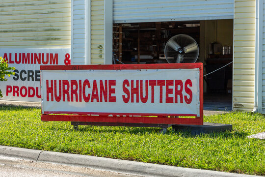 Hurricane Shutters Sign on Grass with a Building in the Background and an Open Garage Style Door