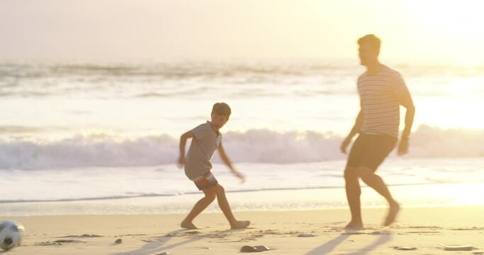 Active father and son playing soccer at the beach at sunset, having fun while keeping fit and bonding. Parent being playful with his child, enjoying a sporty game while spending free time together