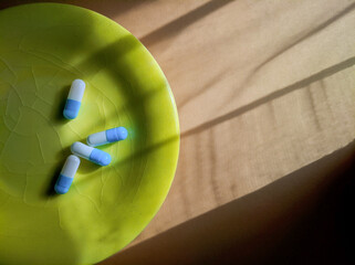 Flat lay photo of blue white capsules on a green plate