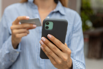 female hands hold a modern mobile phone and a bank credit or debit card on the street..ordering purchases, working online, transferring money by phone