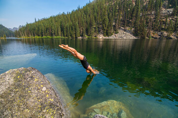 Fototapeta na wymiar Adventurous athletic female hiker diving into an alpine lake in the Pacific Northwest. 