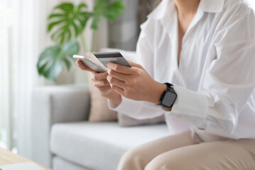 Close up image of young woman holding credit card and using smart phone online shopping, e-commerce, internet banking, spending money, working from home concept.