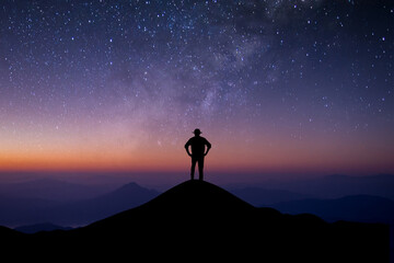 Silhouette of young man standing alone on top of mountain enjoying watching beautiful of night sky,...