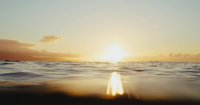 VIew of the sun setting from in the ocean, over under split view, waves rolling in slow motion