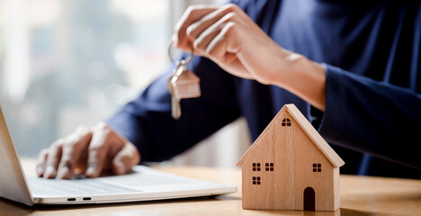 Businessman choosing mini wood house model from model and row of coin money on wood table, selective focus, Planning to buy property. Choose what's the best.