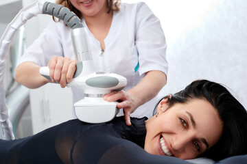 Beautician makes LPG calf massage of legs to young woman in black suit. Lymphatic drainage massage. Slimming treatments