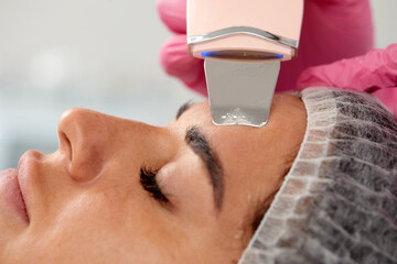 Beauty doctor with ultrasonic scraber doing procedure of ultrasonic cleaning of face. Cosmetology...