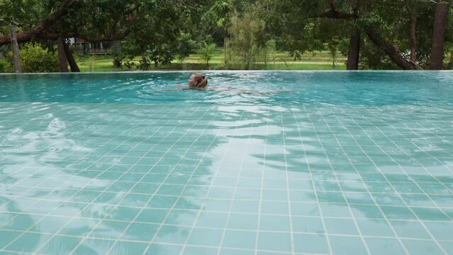 Beautiful long-haired woman swims in an outdoor infinity pool against the backdrop of tropical vegetation, 10 bit prores