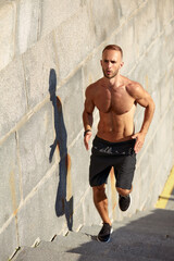 Urban sports. Sporty man shirtless jogging for fitness in the city park on a beautiful summer day