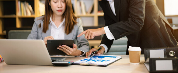 Asian businesswoman hand using laptop and tablet with social network diagram and two colleagues discussing data on desk as concept.