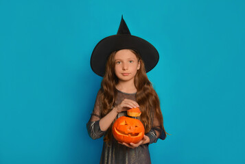 Cute child girl in witch costume holding Halloween pumpkin or Jack o lantern pumpkin and looking at camera on a blue background.

Wizard kid holding top of pumpkin in hands. 