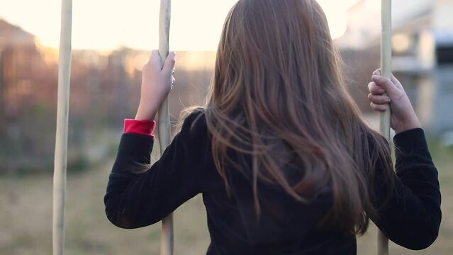 Little girl playing alone on the swings of a swing set hair blowing in the breeze late afternoon sunset b roll