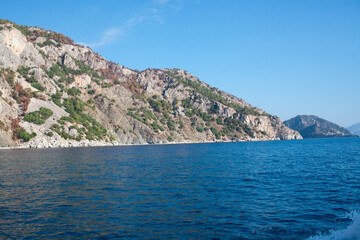 Fototapeta na wymiar Mediterranean rocky shores with green trees and landscape. View from sea. Rock reflection in blue water sea.