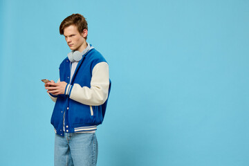  young stylish guy in a bomber and jeans stands with a phone in his hands and headphones around his...