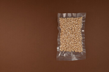Cedar nuts. Peeled pine nuts in transparent vacuum package.  Brown background, copy space