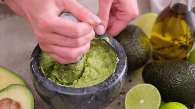 Making guacamole sauce - woman mashing avocado in a marble mortar with pestle at domestic kitchen