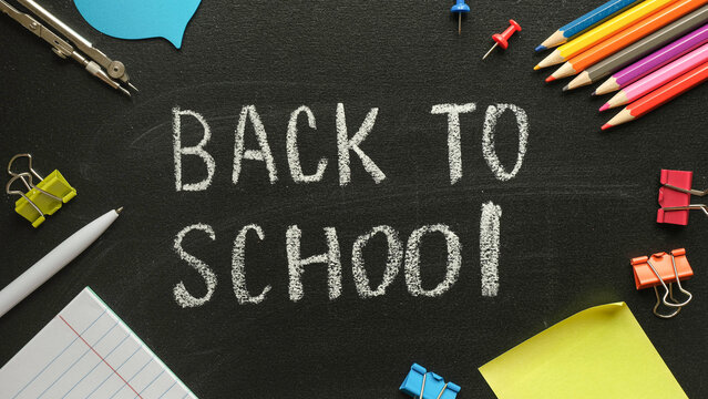Back to school - chalk lettering on a school blackboard with stationery around - pencils, pins, pen, copybook