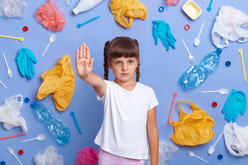 Strict serious little girl wearing white t shirt showing stop sign with palm, calls to solve the...