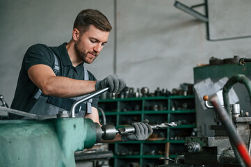 Working with metal. Man in uniform is indoors developing details of agriculture technique