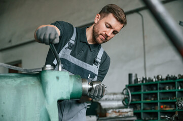 Working with metal. Man in uniform is indoors developing details of agriculture technique